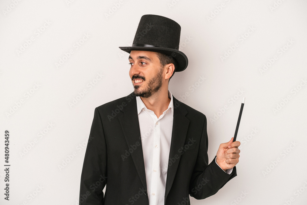 Young magician man holding wand isolated on white background looks aside smiling, cheerful and pleasant. Young magician man holding wand isolated on white background looks aside smiling, cheerful and pleasant.