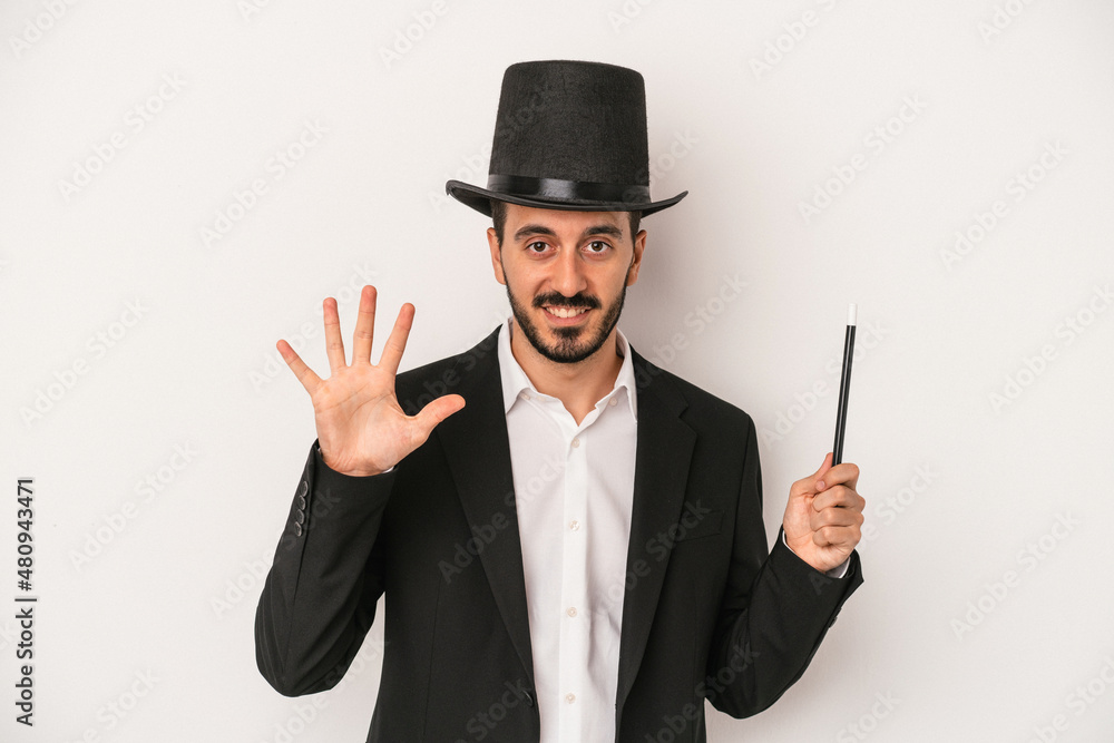 Young magician man holding wand isolated on white background smiling cheerful showing number five with fingers. Young magician man holding wand isolated on white background smiling cheerful showing number five with fingers.