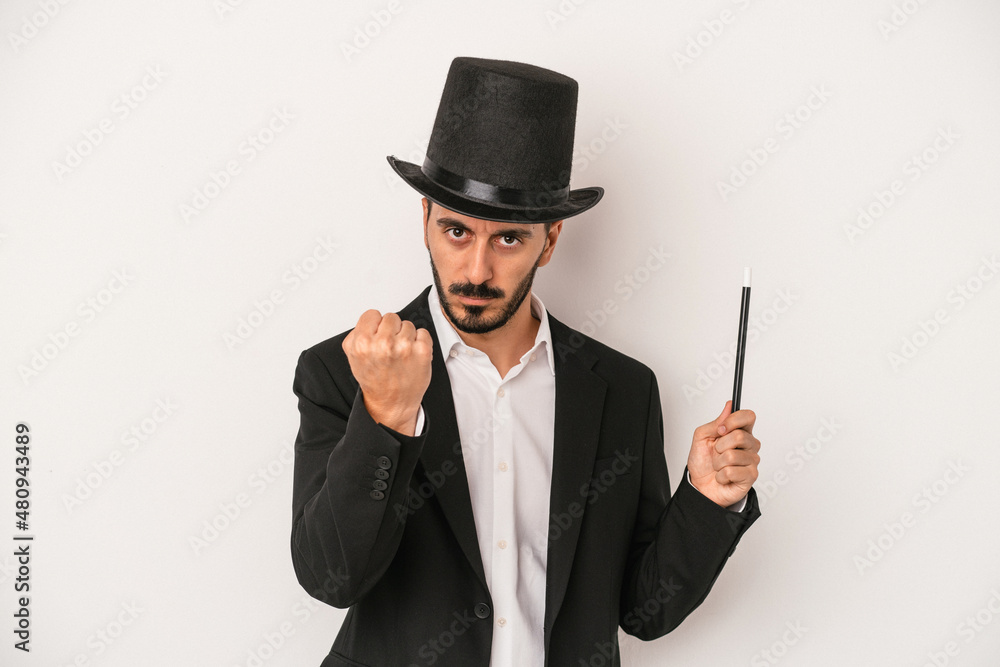 Young magician man holding wand isolated on white background showing fist to camera, aggressive facial expression. Young magician man holding wand isolated on white background showing fist to camera, aggressive facial expression.
