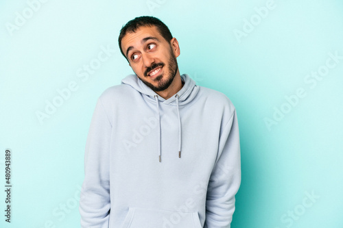 Young caucasian man isolated on blue background laughs and closes eyes, feels relaxed and happy. © Asier