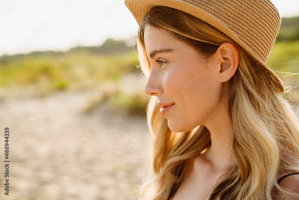 Young blonde woman wearing straw hat smiling and looking aside