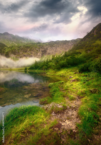 Beautiful footpath by a mountain lake in dramatic light with dark clouds 