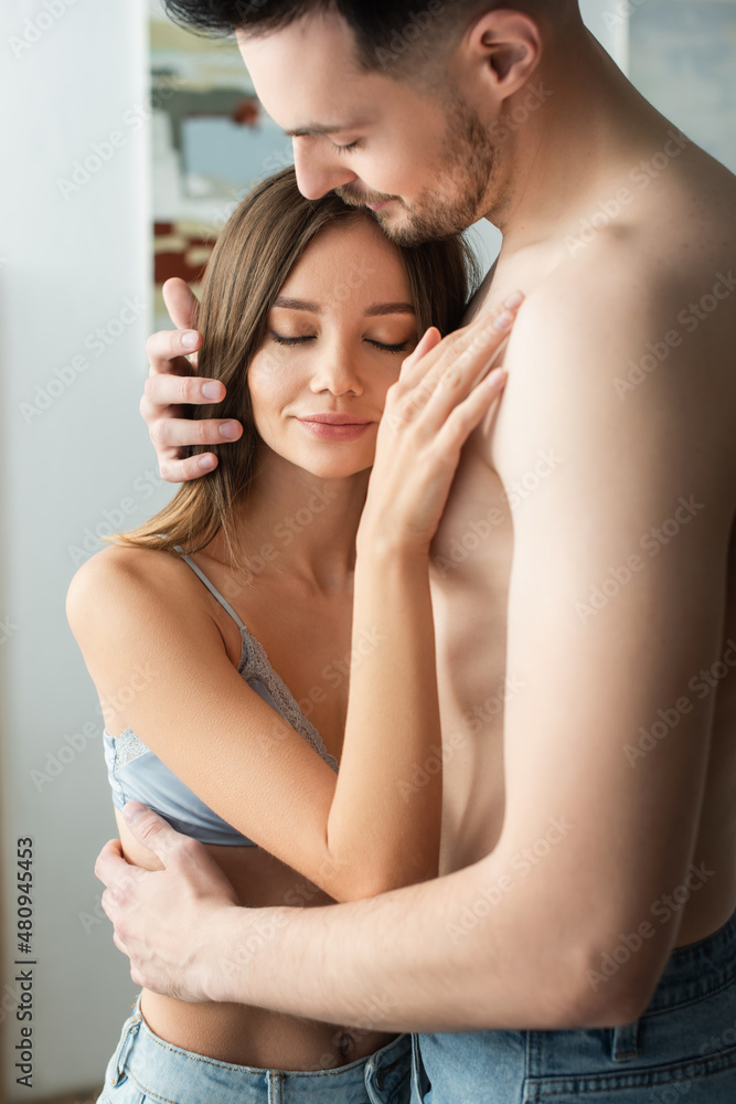 smiling woman with closed eyes leaning on chest of shirtless man while standing in bedroom. smiling woman with closed eyes leaning on chest of shirtless man while standing in bedroom.