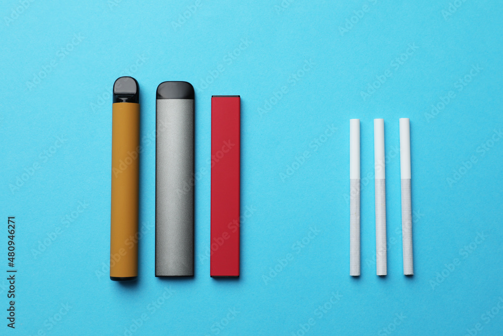 Fototapeta premium Electronic and regular cigarettes on light blue background, flat lay