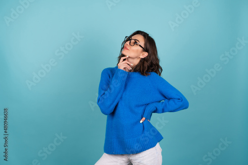 A woman in a blue knitted sweater and natural make-up  curly short hair  looks away thoughtfully  thinking about ideas