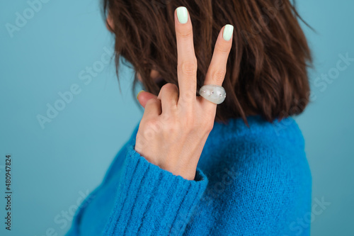 Close shot of a woman's hand in a blue knitted sweater with a large bulky green rhinestone ring and mint spring perfect manicure gel polish on nails