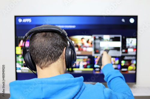 Man in headphones sitting with remote controller on smart TV screen background. Person choosing streaming services, watching movies