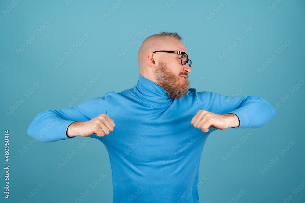 A young man with a red beard in a turtleneck on a blue background is dancing merrily, having fun A young man with a red beard in a turtleneck on a blue background is dancing merrily, having fun