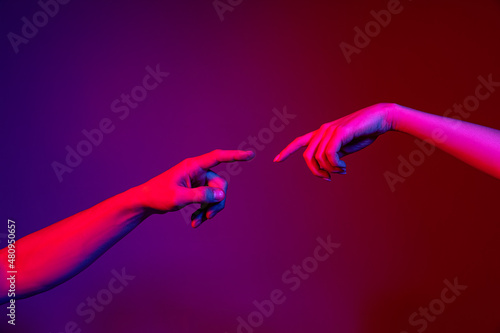 Two human hands trying to touch each other isolated on purple background in neon light. Concept of human relation, community, togetherness, symbolism, culture and history