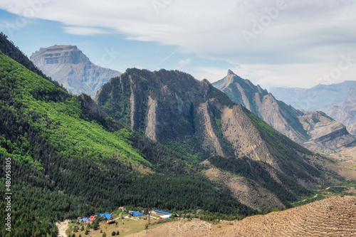 Sharp rocks. Colorful sunny green landscape with silhouettes of big rocky mountains and epic deep gorge with village under the rock.