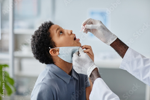 Side view of doctor dropping liquid in mouth of African-American girl during oral vaccination in clinic