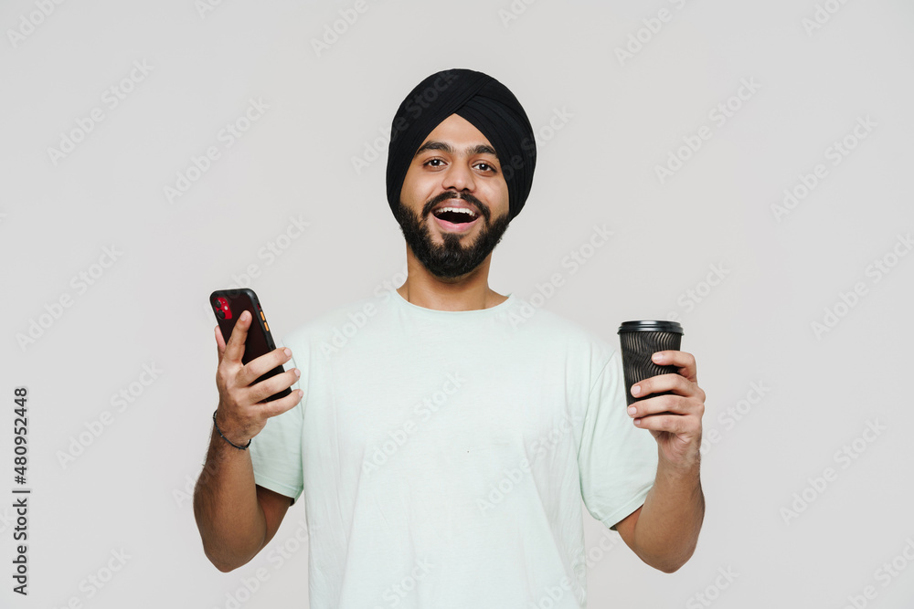 Bearded south asian man using cellphone and drinking coffee Bearded south asian man using cellphone and drinking coffee