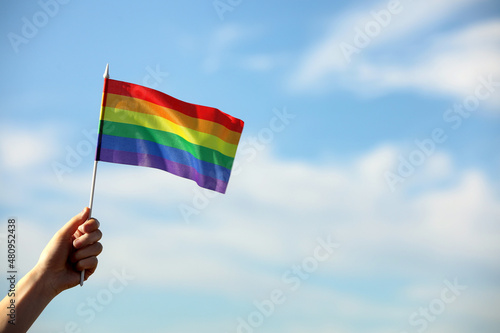 Woman holding bright LGBT flag against blue sky, closeup. Space for text