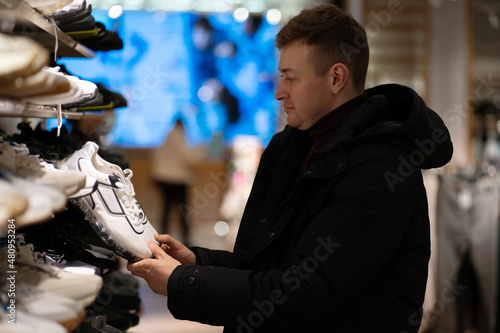 Photo of a handsome brunet young man who chooses sneakers in a store in a mall. Shopping concept