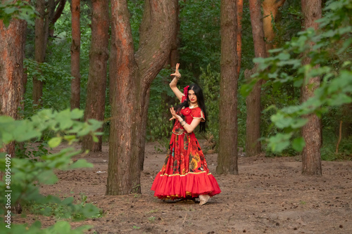 Gypsy woman. Red long dress. Portrait of a girl in an ethnic costume in the forest. The gypsy brunette is beautiful. photo