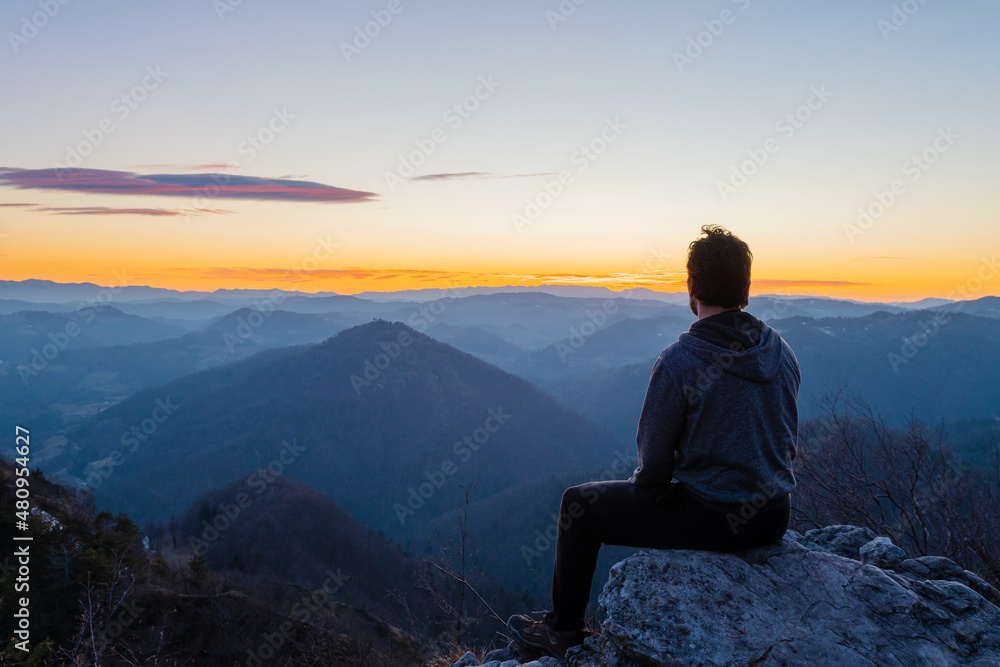 Hiker sitting on top of the hill waiting for sunrise and enjoying scenic view