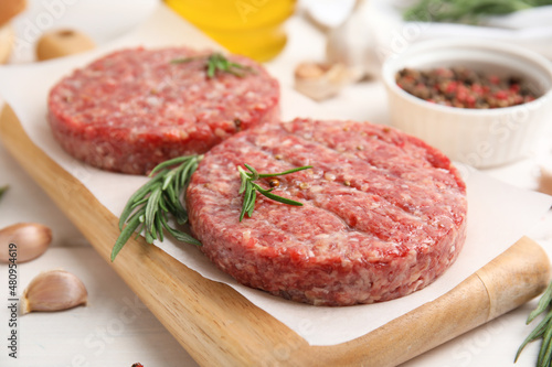 Raw hamburger patties with rosemary on white wooden table, closeup