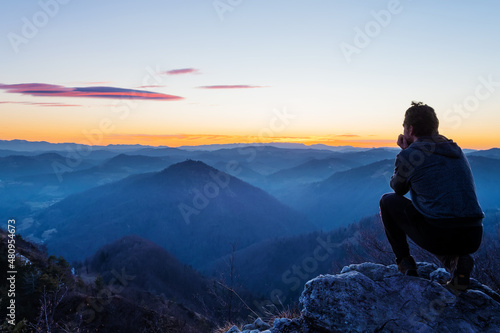 Male hiker crouching on top of the hill watching twilight landscape after sunset © Robert