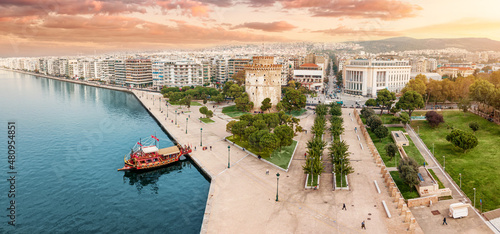 Aerial panoramic view of the main symbol of Thessaloniki city - the White Tower with boat tour ship at the pier. Concept of travel landmarks in Greece and urban development.