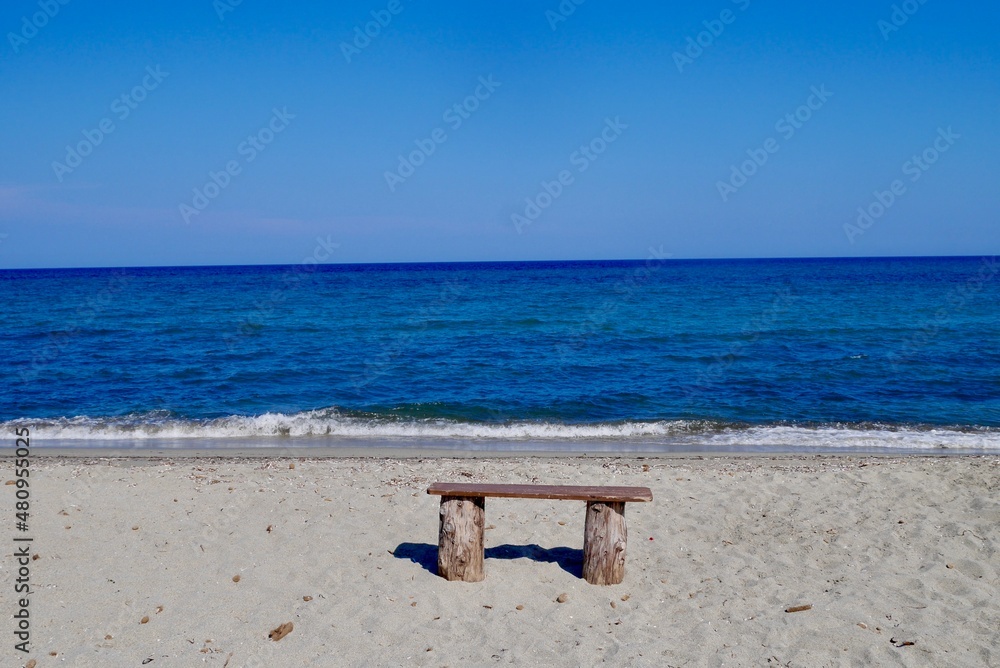 Wooden bench at sandy beach overlooking Mediterranean Sea. Corsica, France.