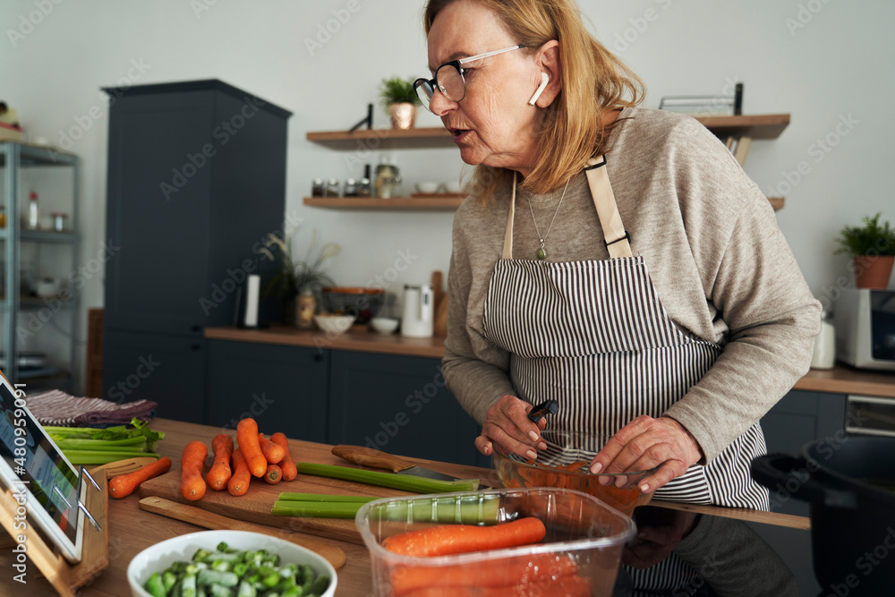 Caucasian senior woman cooking and chatting via earphones