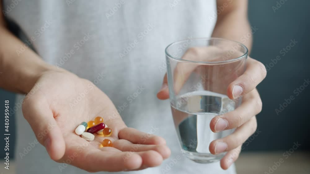 Close-up of male hand holding vitamin pills and glass of water indoors at home. Biologically active supplements and healthcare concept. Close-up of male hand holding vitamin pills and glass of water indoors at home. Biologically active supplements and healthcare concept.