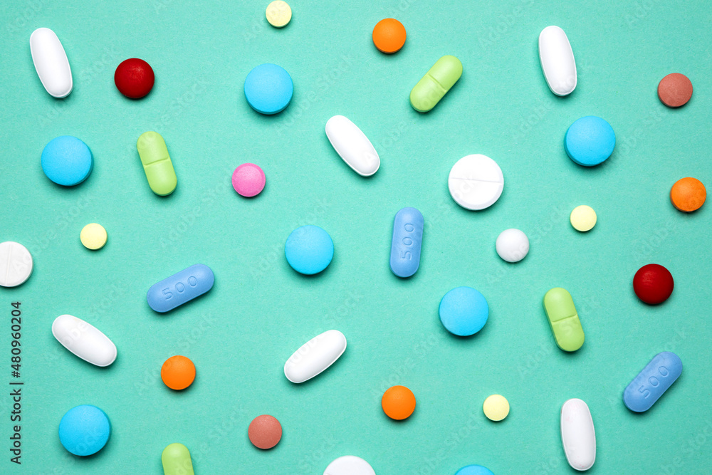 Creative layout of colorful pills and capsules on green background. Minimal medical concept. Pharmaceutical, Covid-19 or Coronavirus. Flat lay.