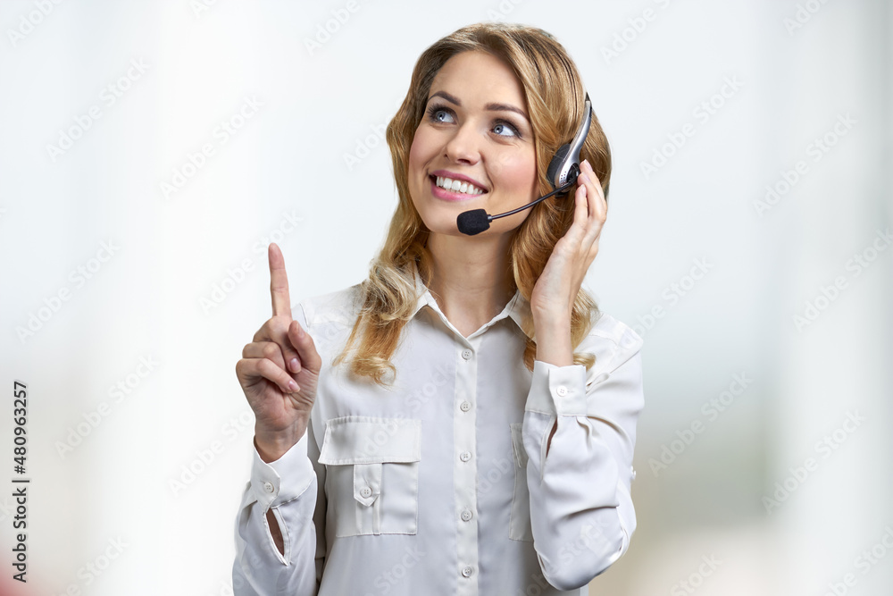 Female phone operator in headset sitting at office and pointing with finger upwards. Female phone operator in headset sitting at office and pointing with finger upwards.