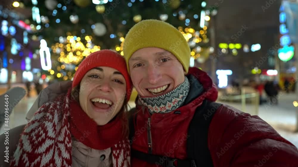 happy couple call their relatives via video link on new year's eve to sound of chimes in middle of street in lights of Christmas market against background. new year and winter holidays concept. happy couple call their relatives via video link on new year's eve to sound of chimes in middle of street in lights of Christmas market against background. new year and winter holidays concept.