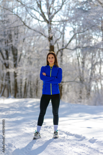 Beautiful Caucasian brunette in sportswear stands on a country road covered with snow and posing for camera. Portrait time