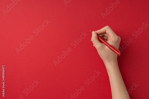 First person top view photo of valentine's day decorations female hand holding red pen on isolated red background with blank space photo
