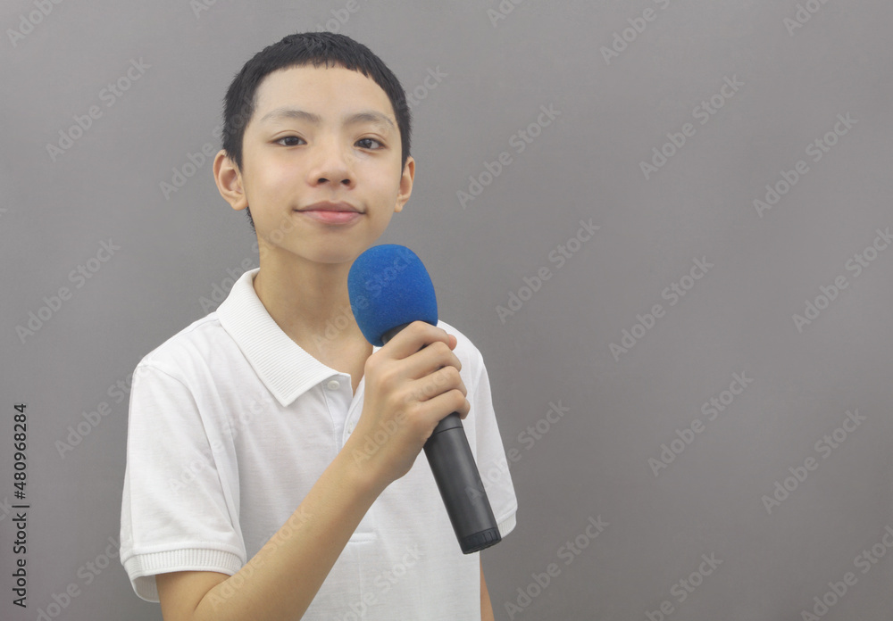 Portrait of confident, handsome and friendly Asian boy holding microphone on gray background. Copy space for text. Portrait of confident, handsome and friendly Asian boy holding microphone on gray background. Copy space for text.
