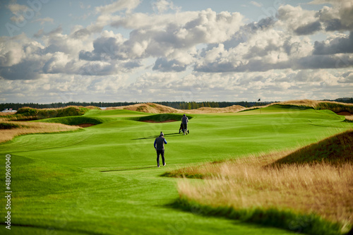 two golfers walk on a green golf course
