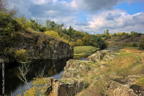 Vertical stone rocks on the bank of the river. A picturesque view of the Tyasminsky canyon with river on sunny day. Kam'yanka Cherkasy region, Ukraine.