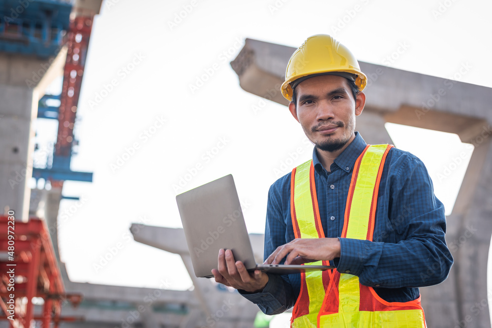 Male engineer holding a laptop computer working at a highway construction site Male engineer holding a laptop computer working at a highway construction site