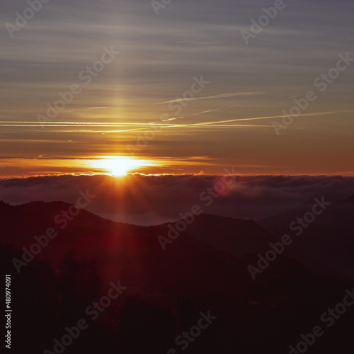 Bright orange sun shining over the clouds on a beautiful morning from the top of a mountain in Montseny Catalonia on a sunrise landscape background