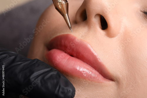 Young woman undergoing procedure of permanent lip makeup in tattoo salon, closeup