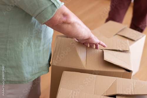 Close-up of elderly man unpacking things in new house. Male hands opening cardboard box. Real estate, purchase concept