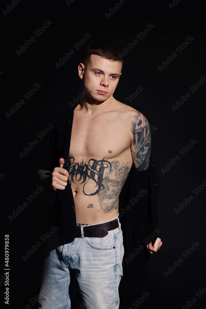 Fototapeta premium Young man with tattoos wearing black shirt on dark background