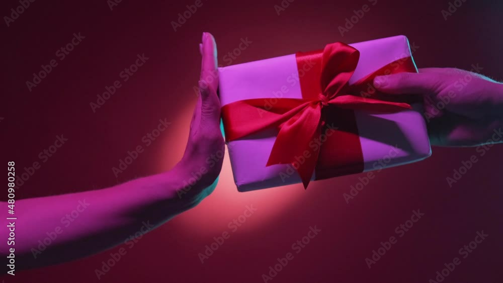 Gift refuse. Couple disagreement. Holidays fail. Female hand protesting to get present with ruby ribbon from male on red purple neon light halo spotlight background. Gift refuse. Couple disagreement. Holidays fail. Female hand protesting to get present with ruby ribbon from male on red purple neon light halo spotlight background.