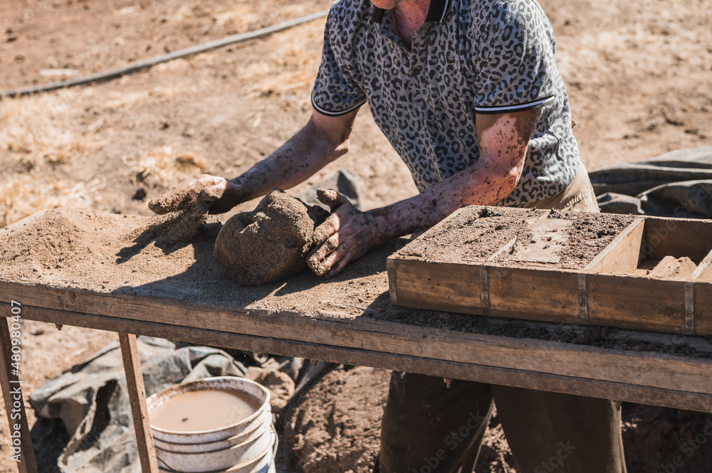 Worker pours the mixture of mud, sand and sawdust over molds for making bricks.