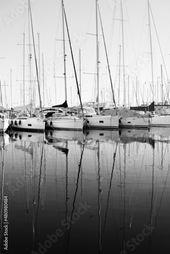 Moored sailboats reflecting their shape in the calm waters of the marina of Varazze, Liguria, Italia. Monochromatic.