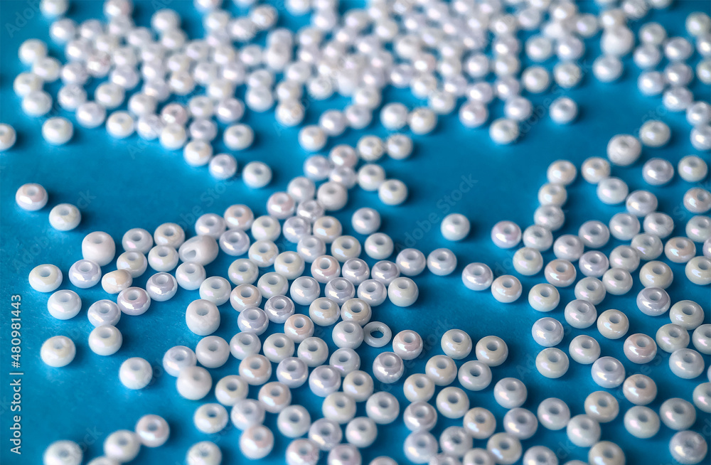 Selective focus, white pearl beads for needlework on a blue background. Making jewelry from beads, embroidery, mosaic and knitting Selective focus, white pearl beads for needlework on a blue background. Making jewelry from beads, embroidery, mosaic and knitting