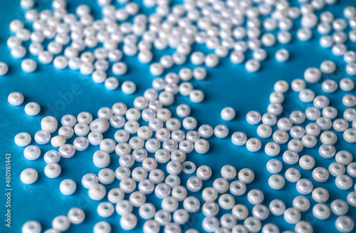 Selective focus, white pearl beads for needlework on a blue background. Making jewelry from beads, embroidery, mosaic and knitting