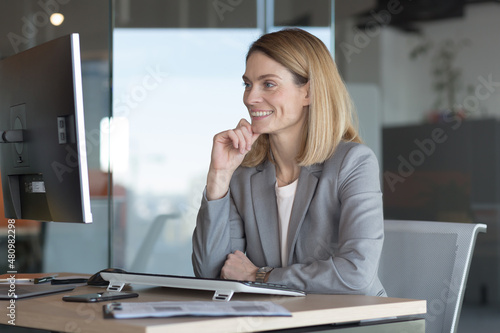 Happy and successful business woman working in the office at the computer rejoices in good results, successful employee and boss