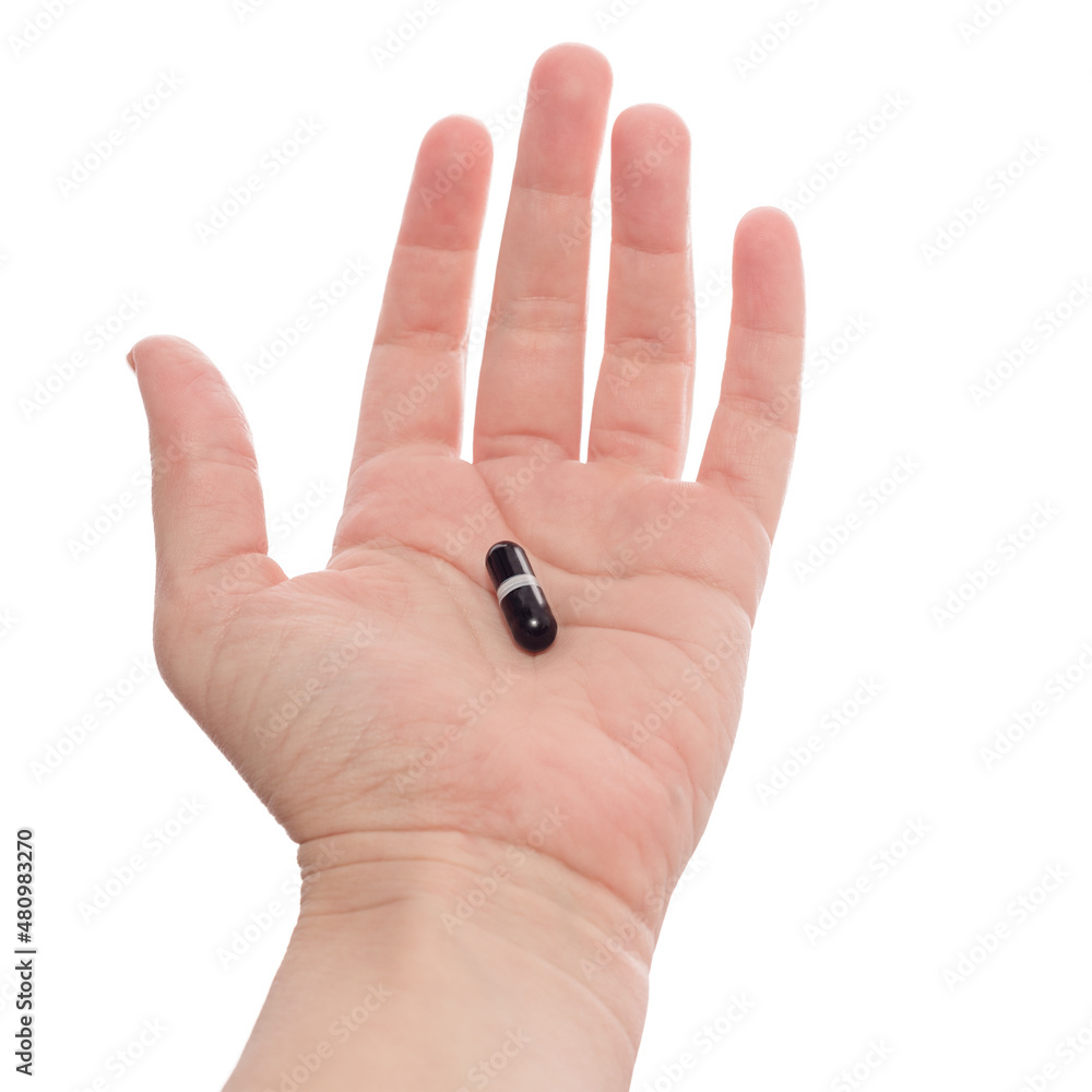 Hand holding or offering black capsule. Isolated on white background. Medicine in palm, medication or a doctor's prescription. Hand holding or offering black capsule. Isolated on white background. Medicine in palm, medication or a doctor's prescription.