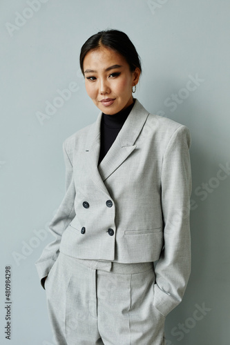 Vertical waist up portrait of beautiful Asian businesswoman wearing suit and looking at camera