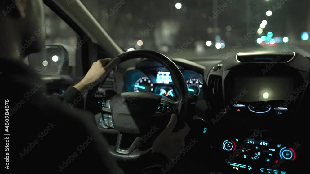 Man driving car through the streets of night city. View from the back seat of the car. Man driving car through the streets of night city. View from the back seat of the car.