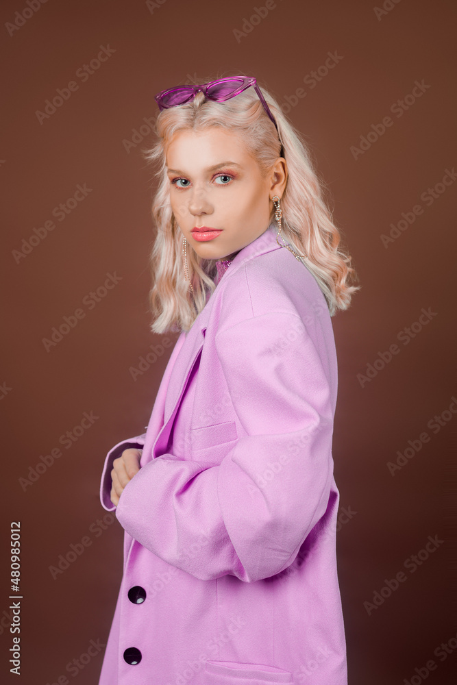 Blonde model in a pink jacket with glasses, a jacket with sequins posing in the studio on a brown background. High fashion, 90s 80s. The girl dances and moves. - obrazy, fototapety, plakaty 