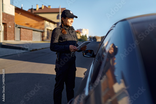 Fotografie Young policewoman with tablet standing near car